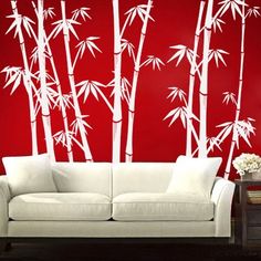 a white couch sitting in front of a red wall with bamboo trees on it's sides