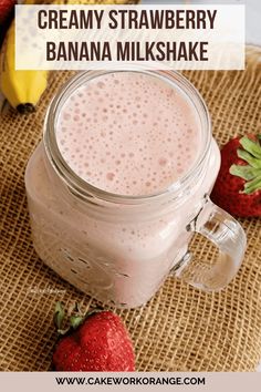 A glass jar filled with a pink strawberry banana milkshake sits on a textured surface, accompanied by fresh strawberries and a banana in the background