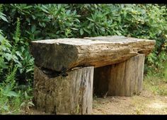 a wooden bench made out of logs sitting in the middle of some grass and bushes