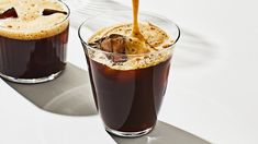 two glasses filled with liquid sitting on top of a white table next to each other