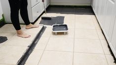 a person standing on the kitchen floor next to a piece of black tile