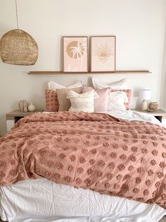 a bed with pink comforter and pillows in a bedroom next to two pictures on the wall