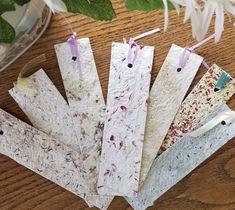 five pieces of paper are sitting on a table next to some flowers and leaves with tags hanging from them