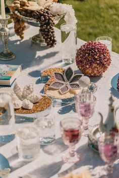 a table topped with lots of plates and glasses filled with food sitting on top of a white table cloth