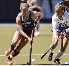 two girls are playing field hockey on the field