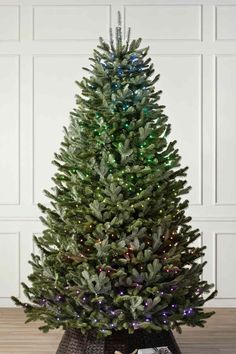 a small christmas tree with lights on it in front of a white wall and wooden floor