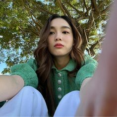 a young woman sitting under a tree with her hands on her hips and looking at the camera