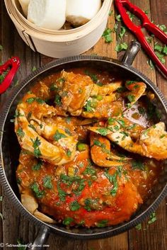 some food is in a pan on a wooden table with red peppers and other items