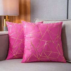 two pink pillows sitting on top of a gray couch next to a light brown lamp