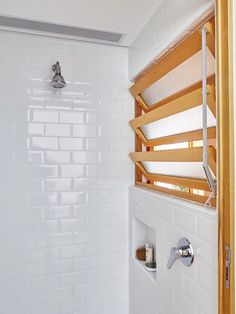 a bathroom with white tile and wooden shelves on the shower wall next to the toilet