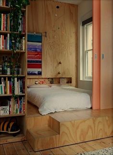 a bed sitting on top of a wooden platform next to a book shelf filled with books