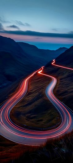 a winding road in the middle of mountains at night with long exposure and light trails