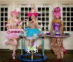 three women dressed in colorful costumes standing next to each other near a table with decorations on it