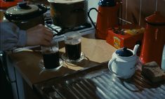 two people are preparing drinks on the stove in their kitchen, one person is holding a mug