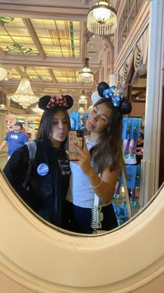 two girls are standing in front of a mirror with mickey mouse ears on their heads