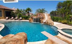 a pool with a slide in it next to some rocks and trees on the other side