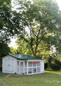 a small white shed sitting in the middle of a field next to a large tree