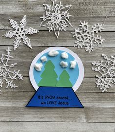 paper snow globe with trees and clouds in it on a wooden table surrounded by snowflakes