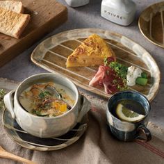 a bowl of soup and two cups on a table with bread, lemon wedges and other food items