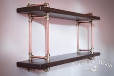 two wooden shelves with metal pipes on the top and bottom, against a pink wall