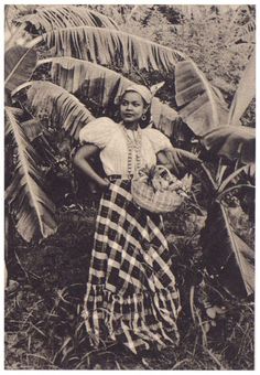 an old black and white photo of a woman standing in front of banana trees holding a basket