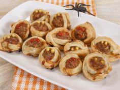 a white plate topped with mini pastries covered in meat and pepper toppings next to a spider