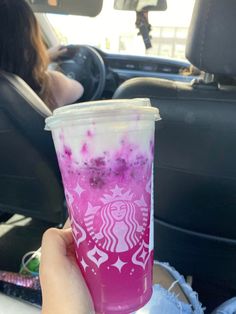 a person holding up a pink and purple drink in the back seat of a car