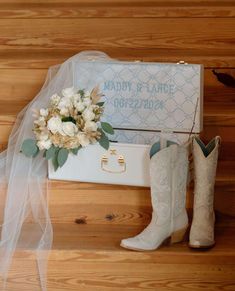 a bouquet of flowers sits on top of a white suitcase next to boots and a wedding ring box