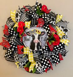 a black and white cow with red flowers on it's deco mesh wreath that says moo y'all