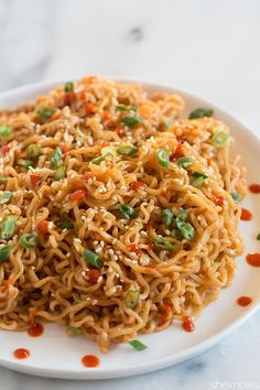 a white plate topped with noodles covered in sauce and green onions next to a fork