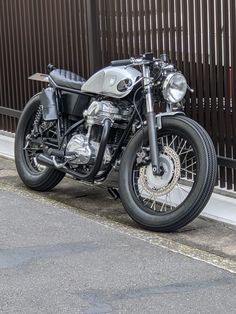 a black motorcycle parked on the side of the road next to a fence and building