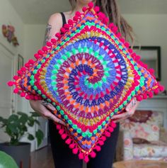 a woman holding a colorful crocheted pillow in her hands