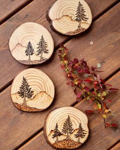 three wood slices with trees on them sitting on top of a wooden table next to flowers