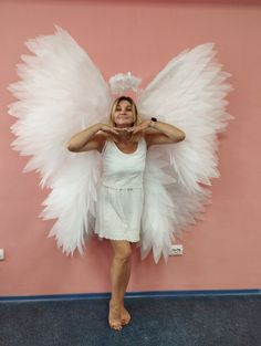 a woman dressed as an angel standing in front of a pink wall with her hands on her hips