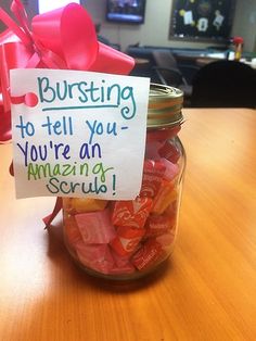 a jar filled with lots of candy sitting on top of a wooden table next to a sign