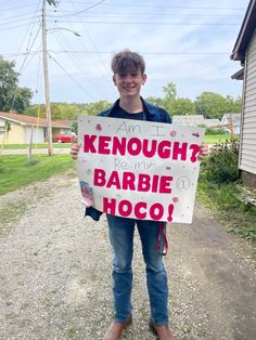 a young man holding a sign that says, i am not kenough? because my barbie is hoco