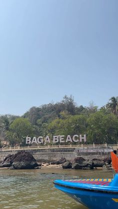 a blue and yellow boat is in the water near a sign that reads baga beach