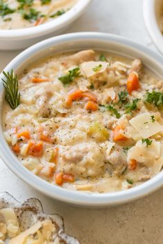 two white bowls filled with chicken and dumpling soup on top of a marble table