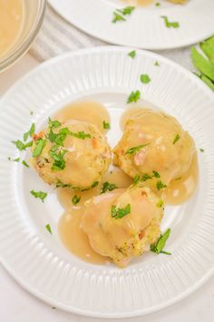 two white plates topped with food covered in gravy next to a bowl of sauce