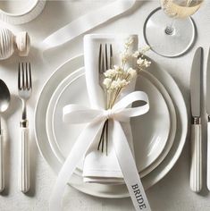 a table setting with white plates, silverware and ribbon tied around the place settings