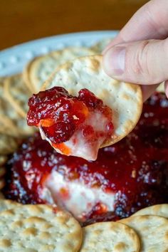 a cracker being dipped with cranberry sauce over crackers on a plate