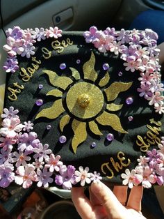 someone is holding up a graduation cap decorated with purple flowers and gold sunburst