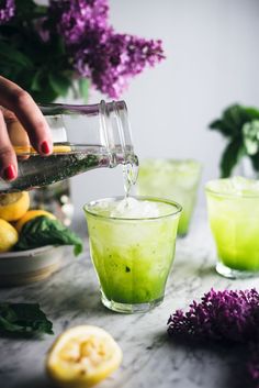 someone pouring something into a glass with lemons and purple flowers in the back ground