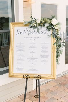 a wedding seating sign with flowers and greenery on it in front of a building