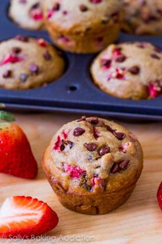 a muffin with chocolate chips and strawberries next to it on a cutting board