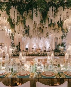 an elegant wedding setup with white flowers and greenery hanging from the ceiling, surrounded by candles