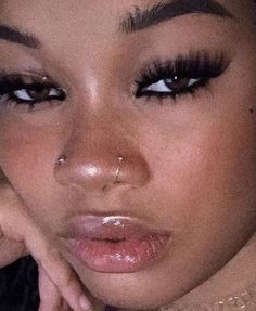 a close up of a woman with her hand on her cheek and nose piercings