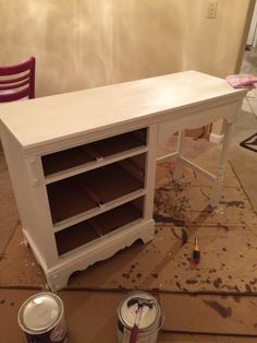 two paint cans are sitting on the floor next to a white table with drawers and shelves