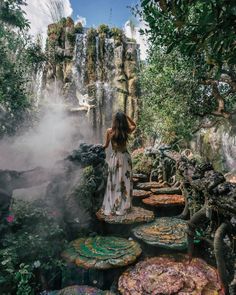 a woman standing in front of a waterfall surrounded by water lilies and other plants