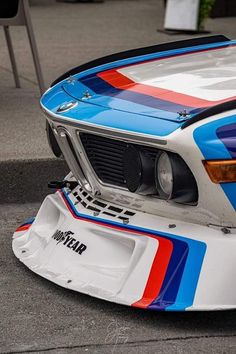 the front end of a bmw race car painted in blue, red and white stripes